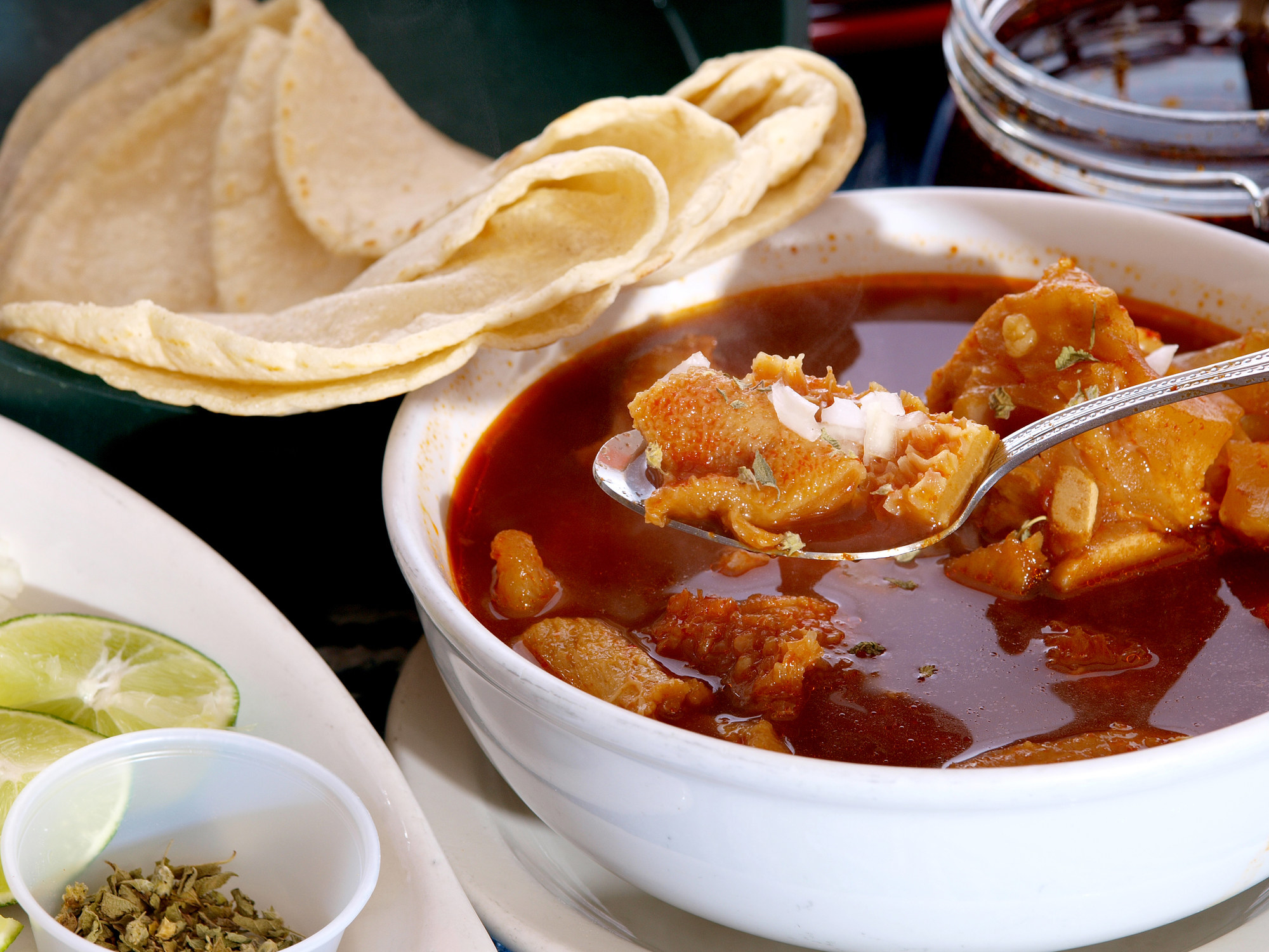 A bowl of menudo soup with a fresh tortilla.