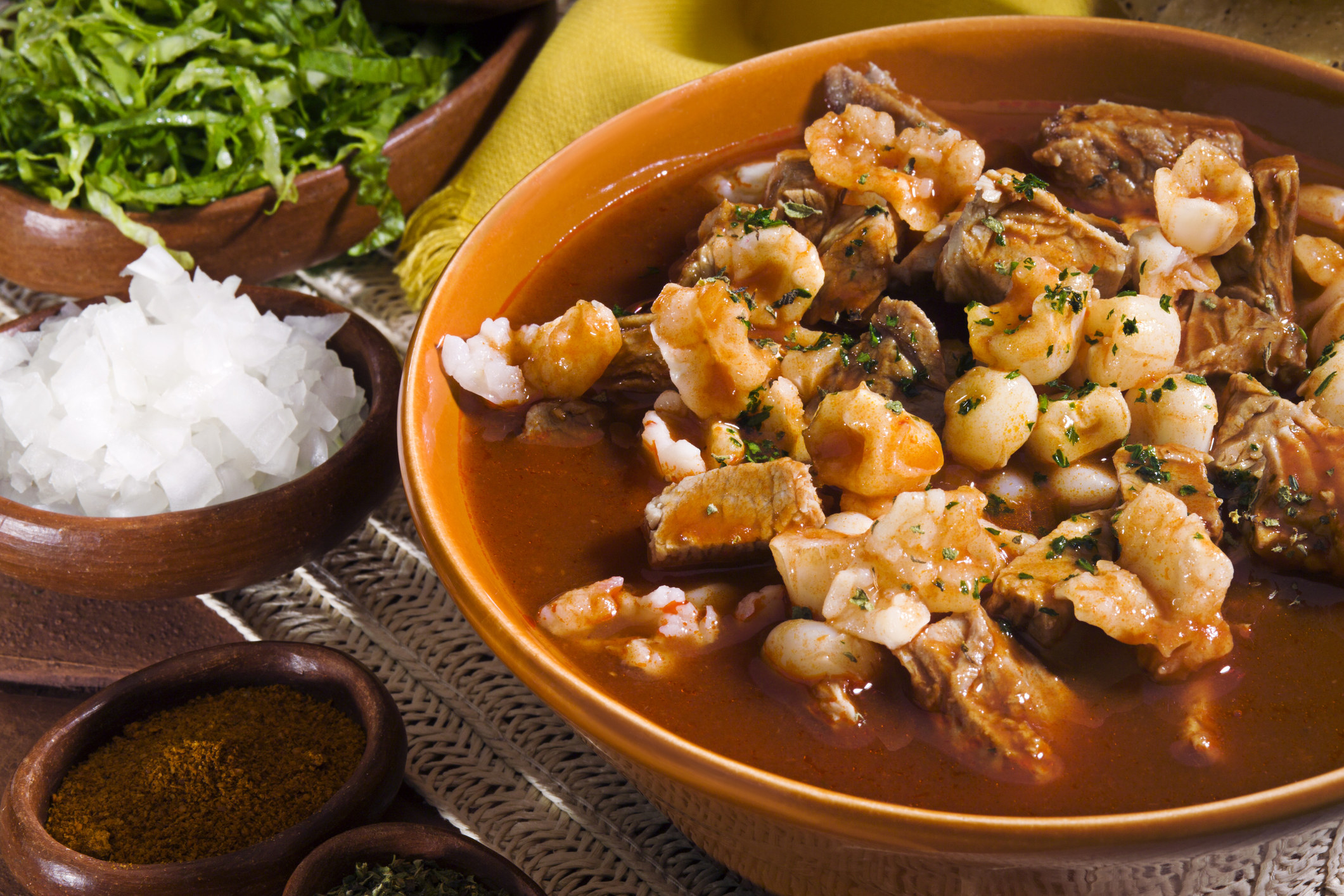 A bowl of pozole with chopped onion and spices.