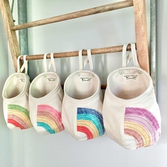 white canvas storage pods with rainbow designs hanging on wooden ladder
