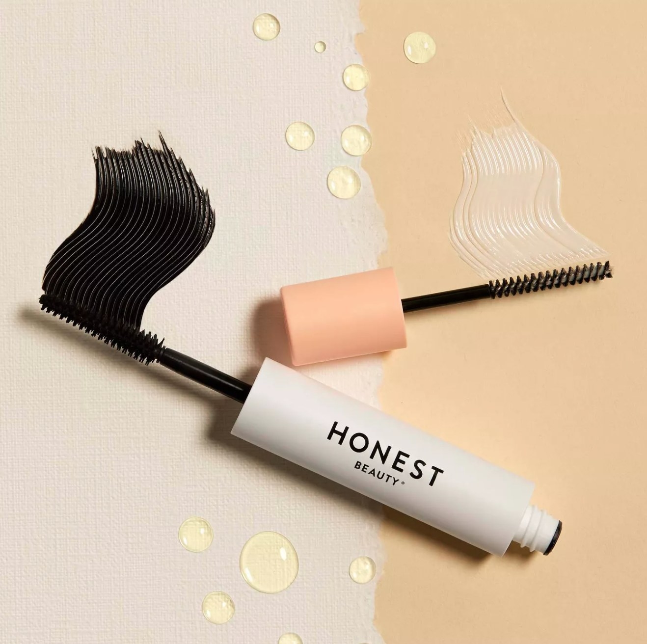 the product with the black mascara side on a cream background with a smudge of mascara and the white primer side on a tan background with a white smudge