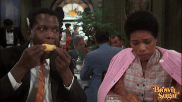 Actor Sidney Poitier eats corn while a woman sits behind him looking nervous.