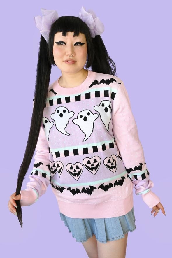 a model wearing the pastel pink, blue, and purple sweater with ghost, bat, and pumpkin heart detailing