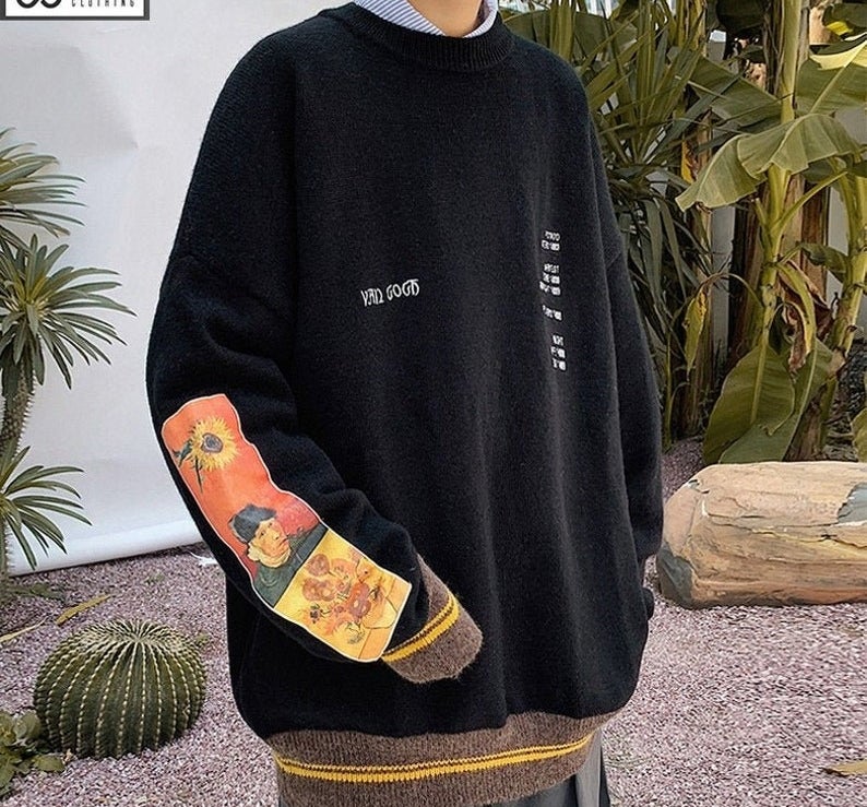 a model wearing the black sweater with painting on one sleeve and a color-blocked hem