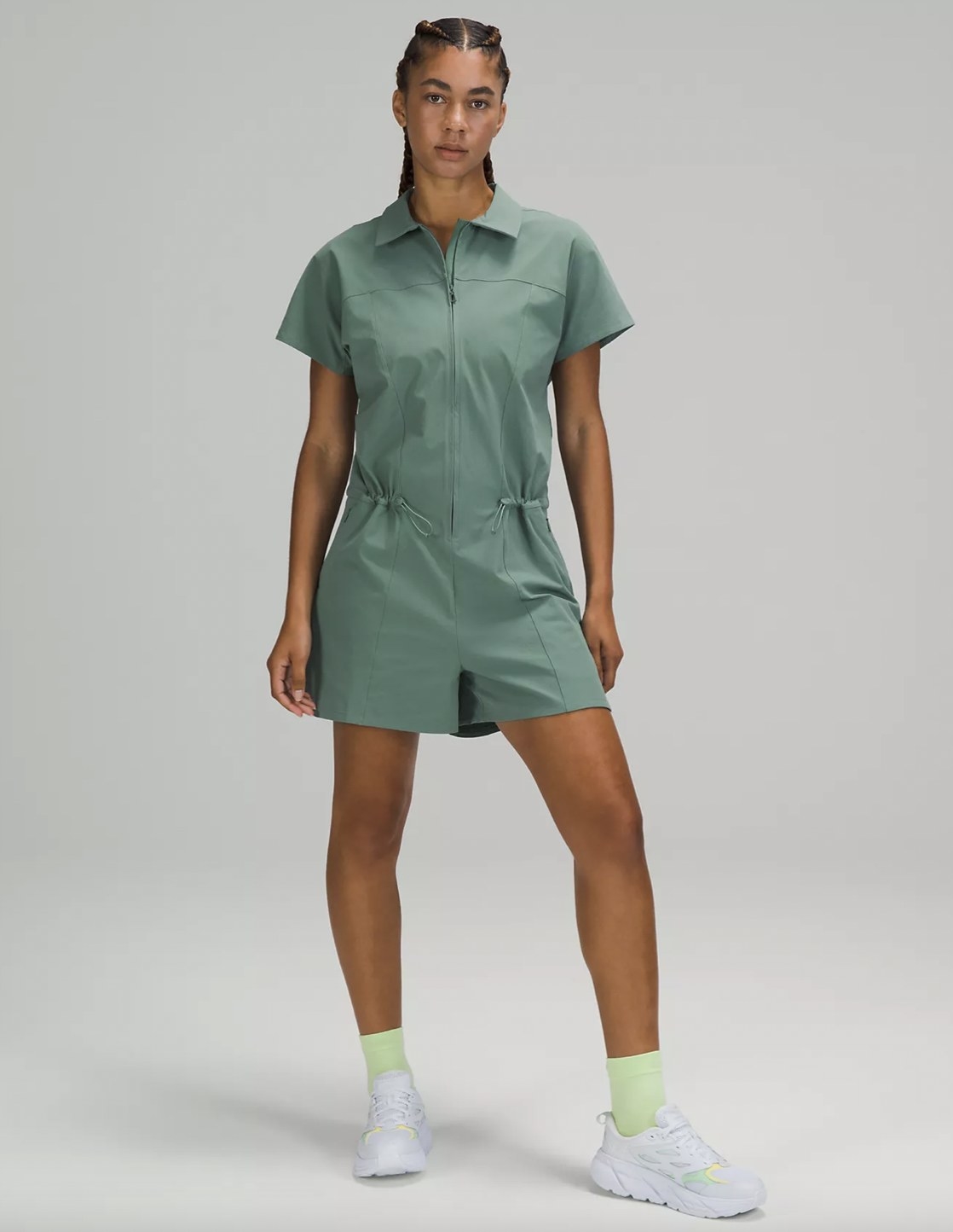 A woman wearing a green romper with white and lime green sneakers