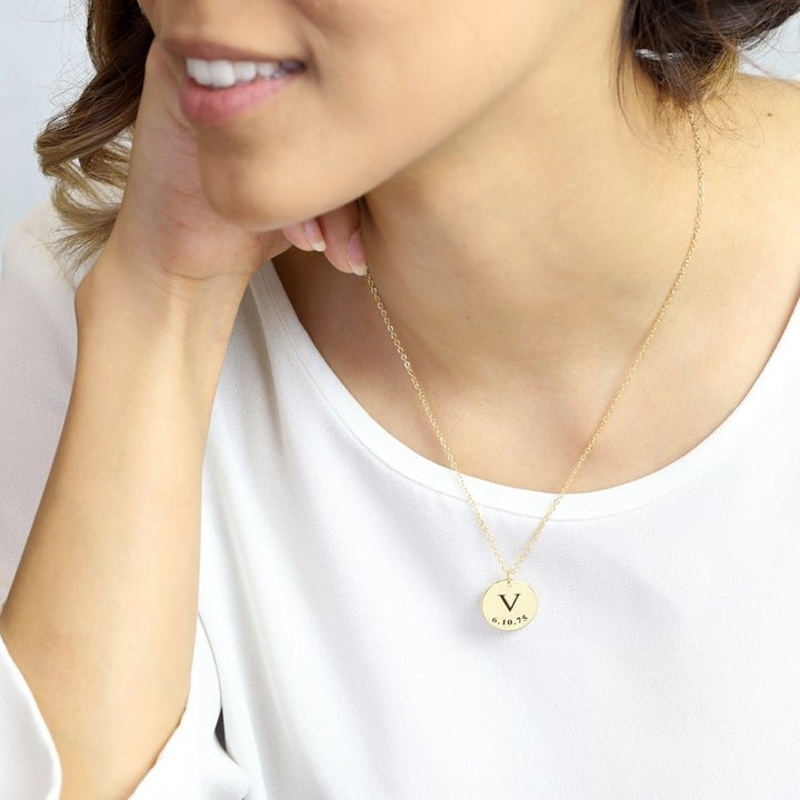 model wearing the gold necklace which has a thin chain and a charm with the initial "V" and a date engraved