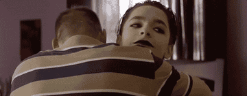 A boy wearing goth makeup gets hugged by another boy whose back is to the camera.