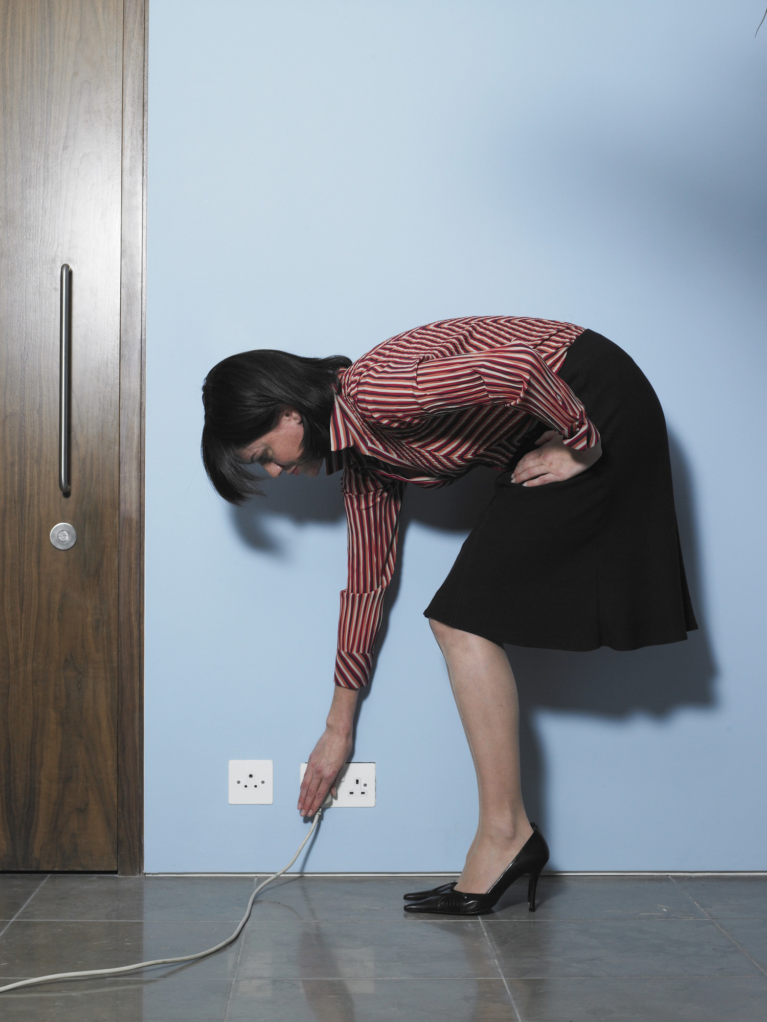 A woman bending down to plug something into the wall