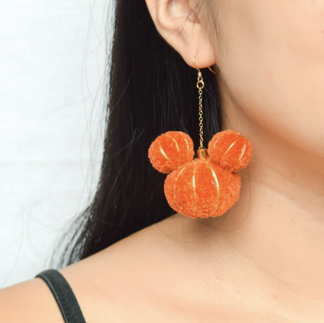 Person wearing fluffy bear-shaped pumpkin earring.