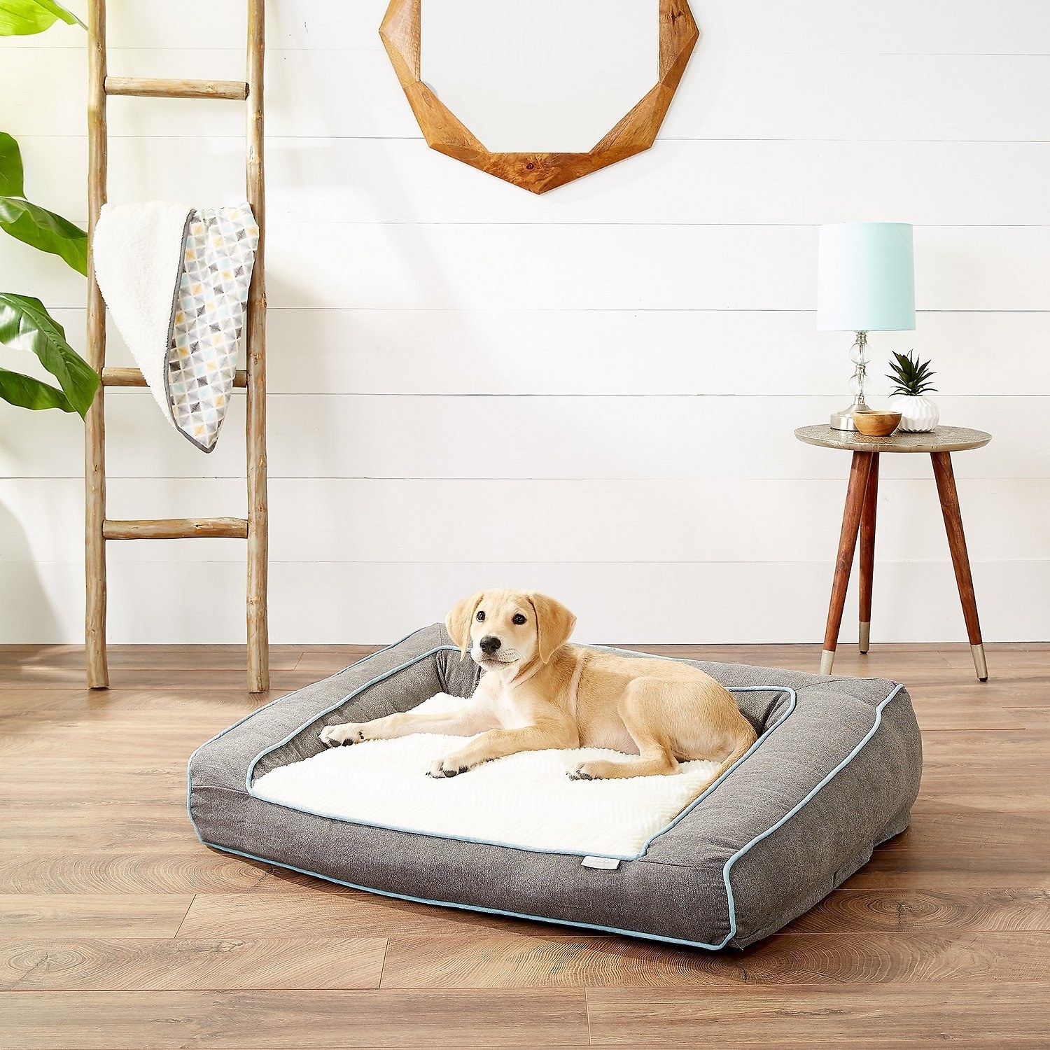 gray and white  dog bed with slanted side bolsters and a puppy on it