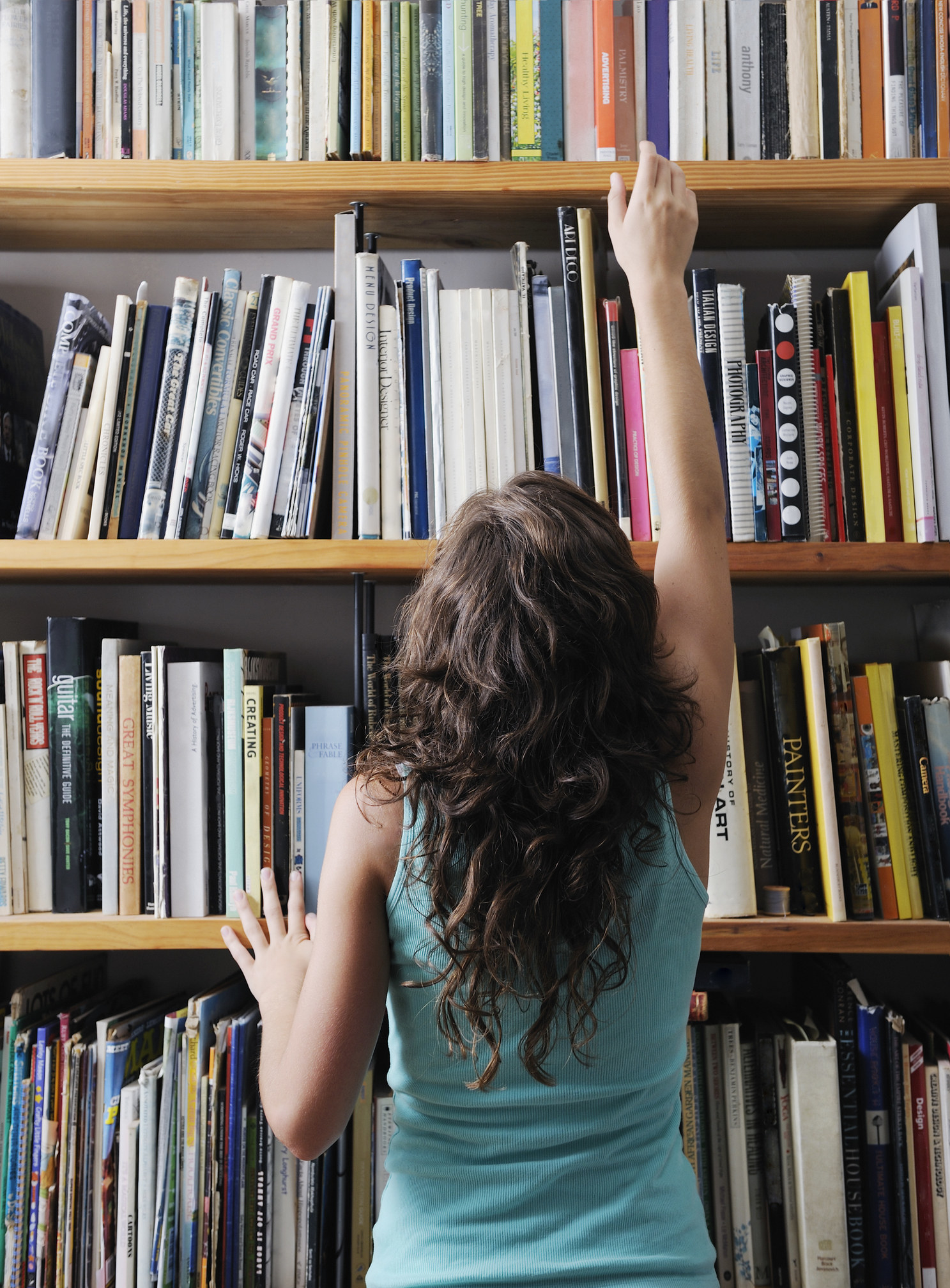 A woman reaching for a book on a shelf