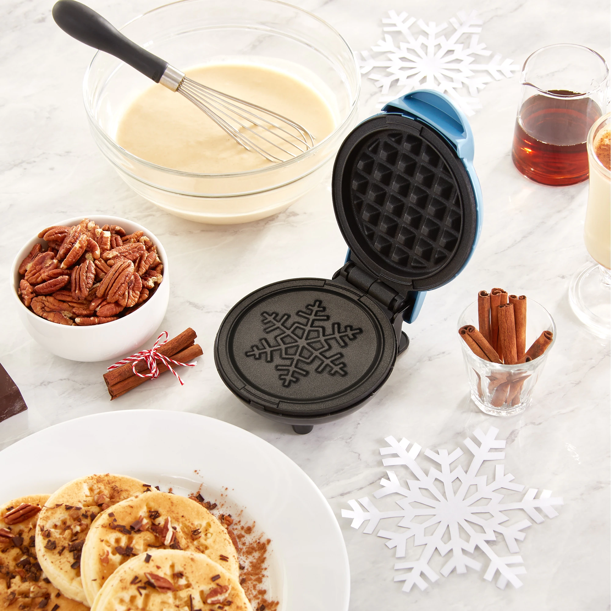 A small waffle maker next to a plate of fresh waffles