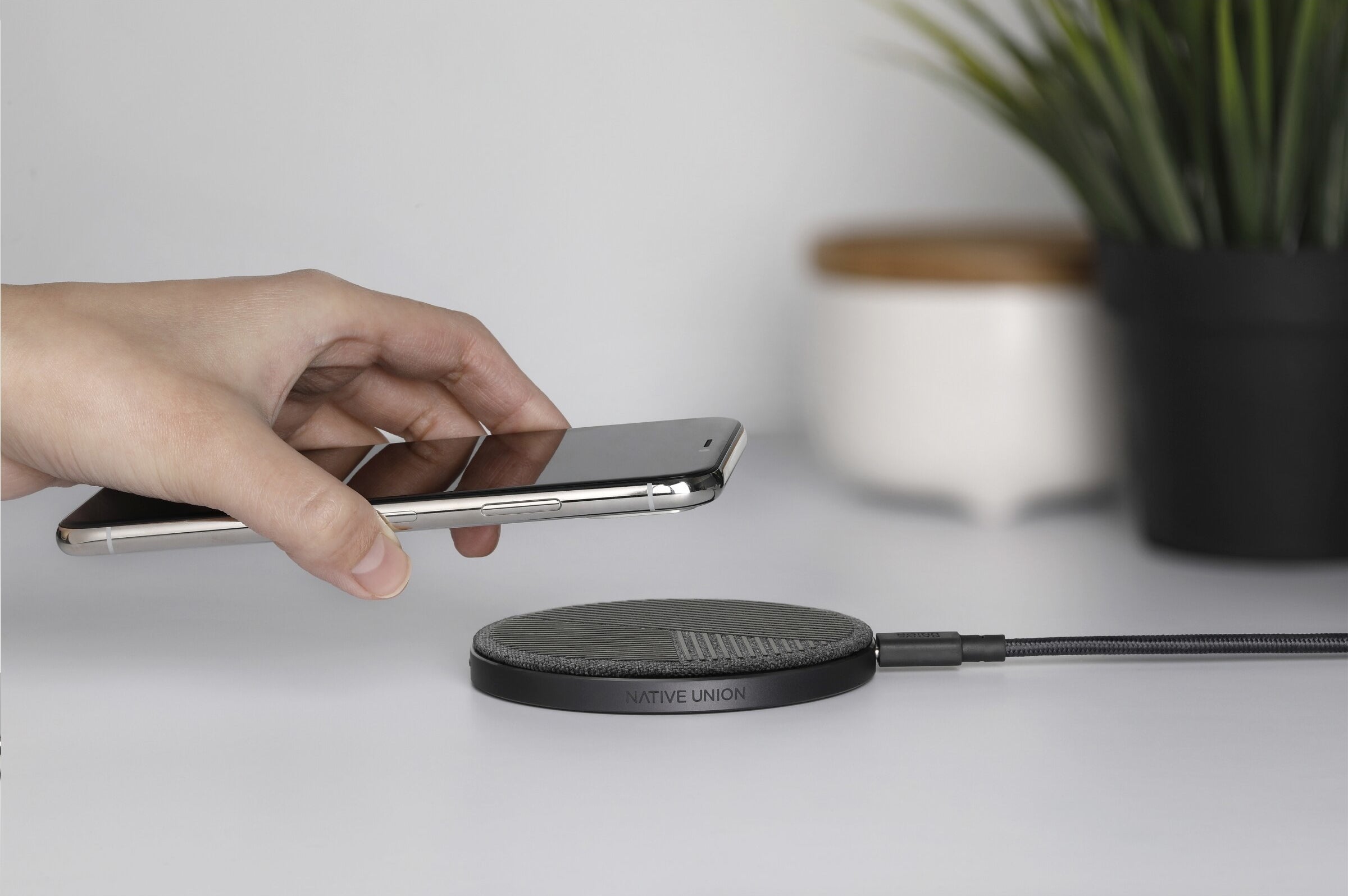 A person placing their phone on a flat round wireless charging base with a cord