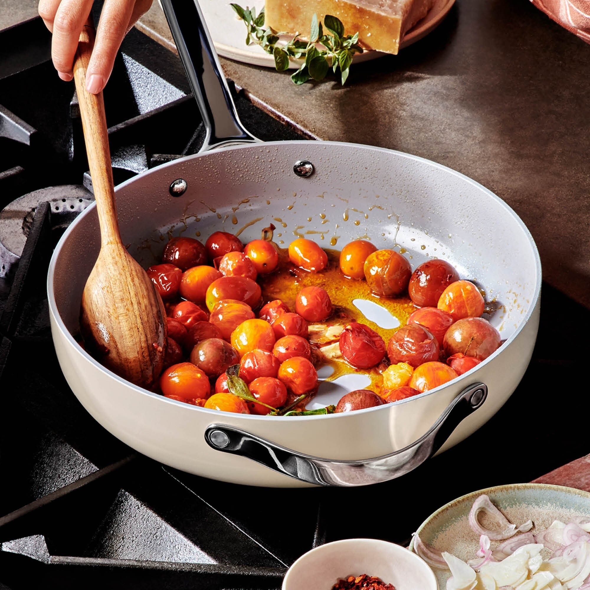 A person cooking cherry tomatoes in a large saute pan