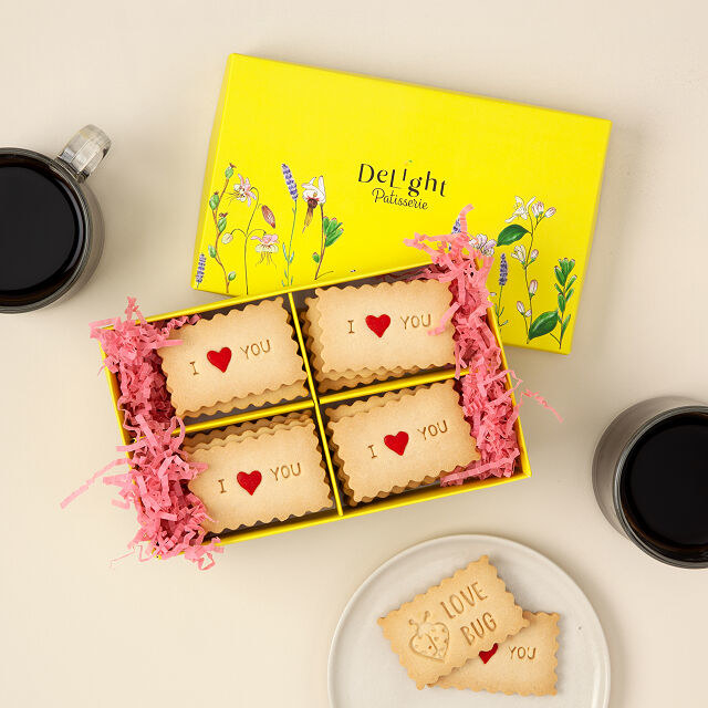 Product image of yellow box with cookies that say "I love you" and a plate with a cookie saying "love bug"
