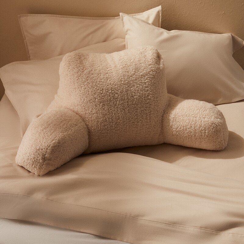 A large pillow with arms lying on a bed