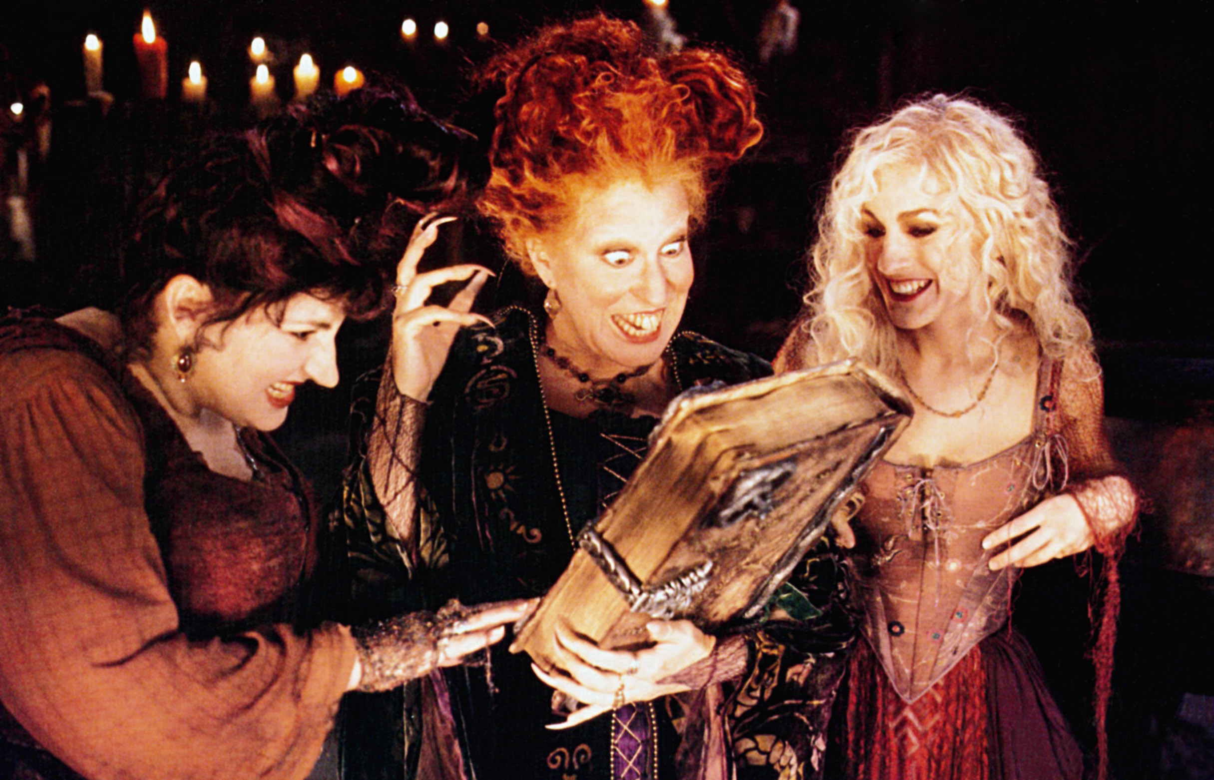 Kathy Najimy, Bette Midler, and Sarah Jessica Parker looking excitedly at a book