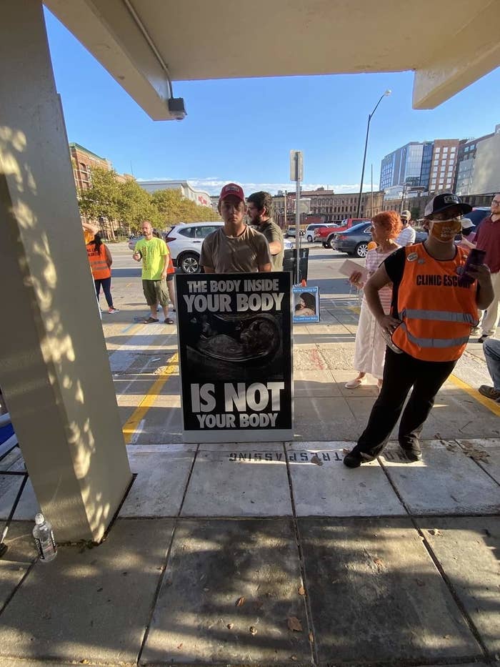 Person holds a sign reading "The body inside your body is not your body" next to a clinic escort