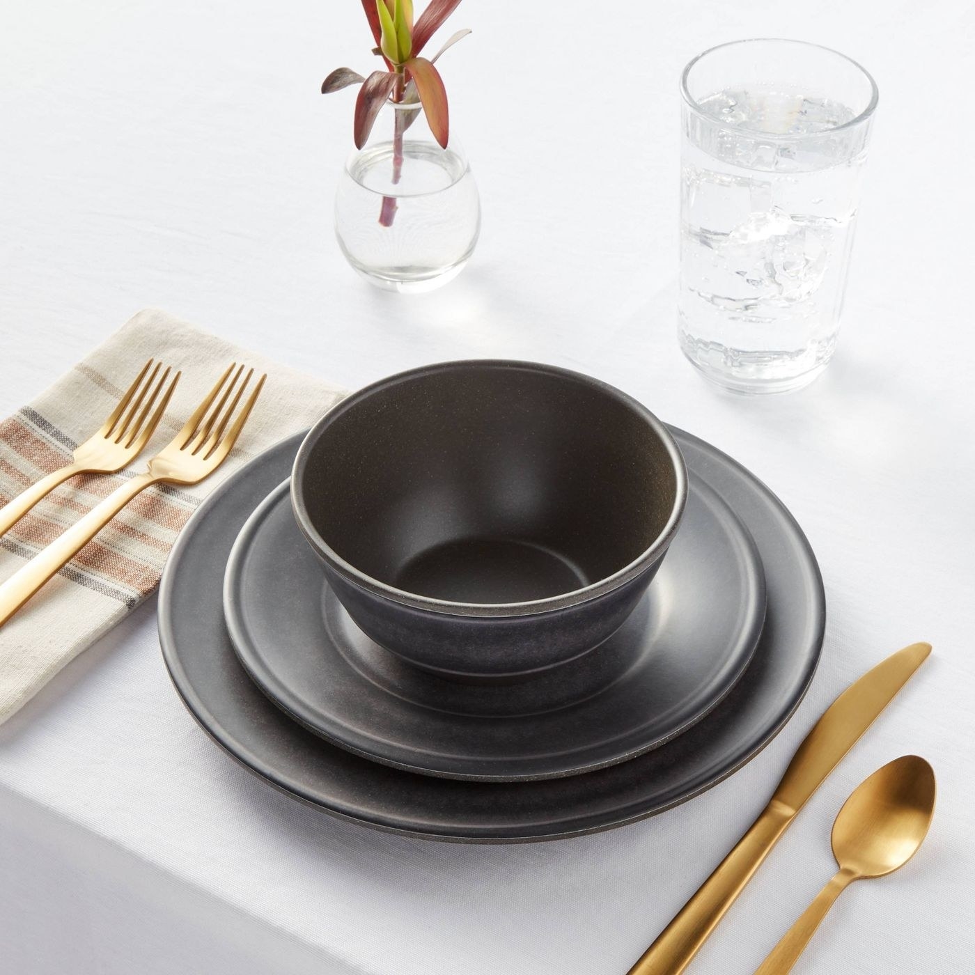 A grey set of dishes on a table with gold silverware
