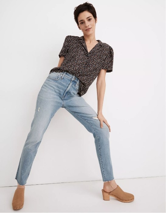 Model wearing black floral short sleeve blouse with jeans and clogs
