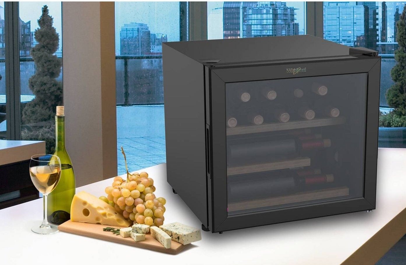 A small wine fridge on a table with wine and cheese plate