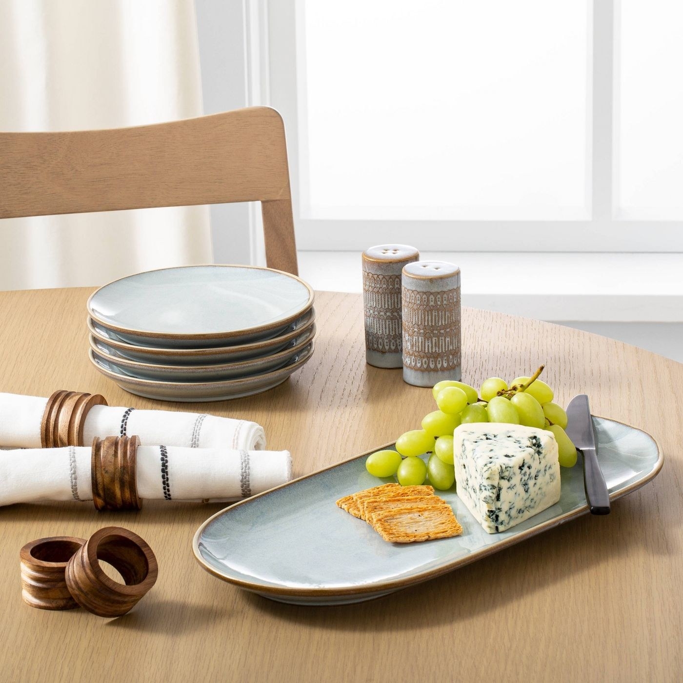 Wood napkin rings on napkin with a cheese plate, plates and salt and pepper shaker