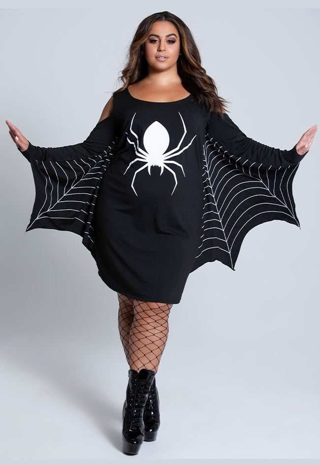 a model wearing fishnet stockings and a black dress with a spider print on the front and a web print on the sleeves