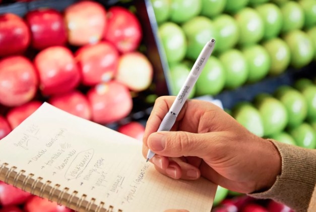 A hand using the pen to check off a grocery list