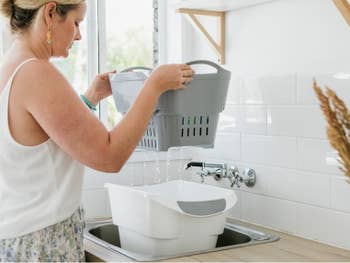 model pulling gray strainer bucket out of larger white bin in a sink