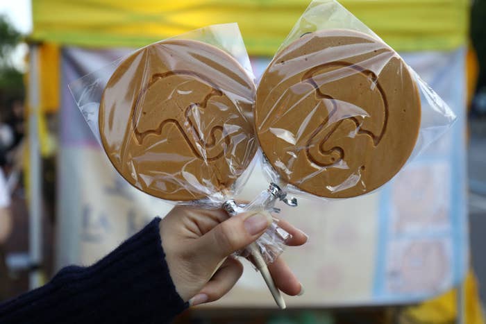 Person holding up two wrapped dalgona candies on lollipop sticks