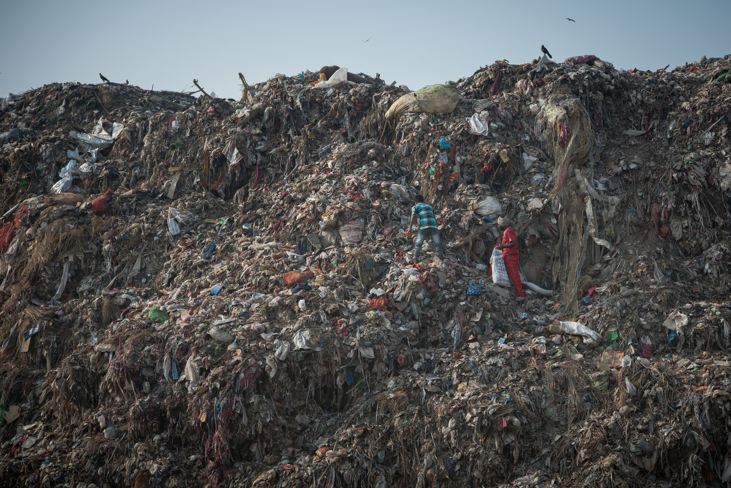 Two people are seen climbing a mountain of trash in India 