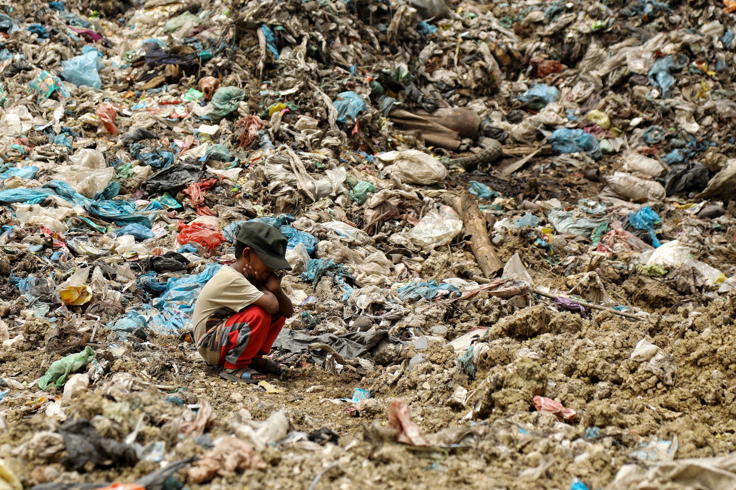 A young boy sits among trash in a landfill