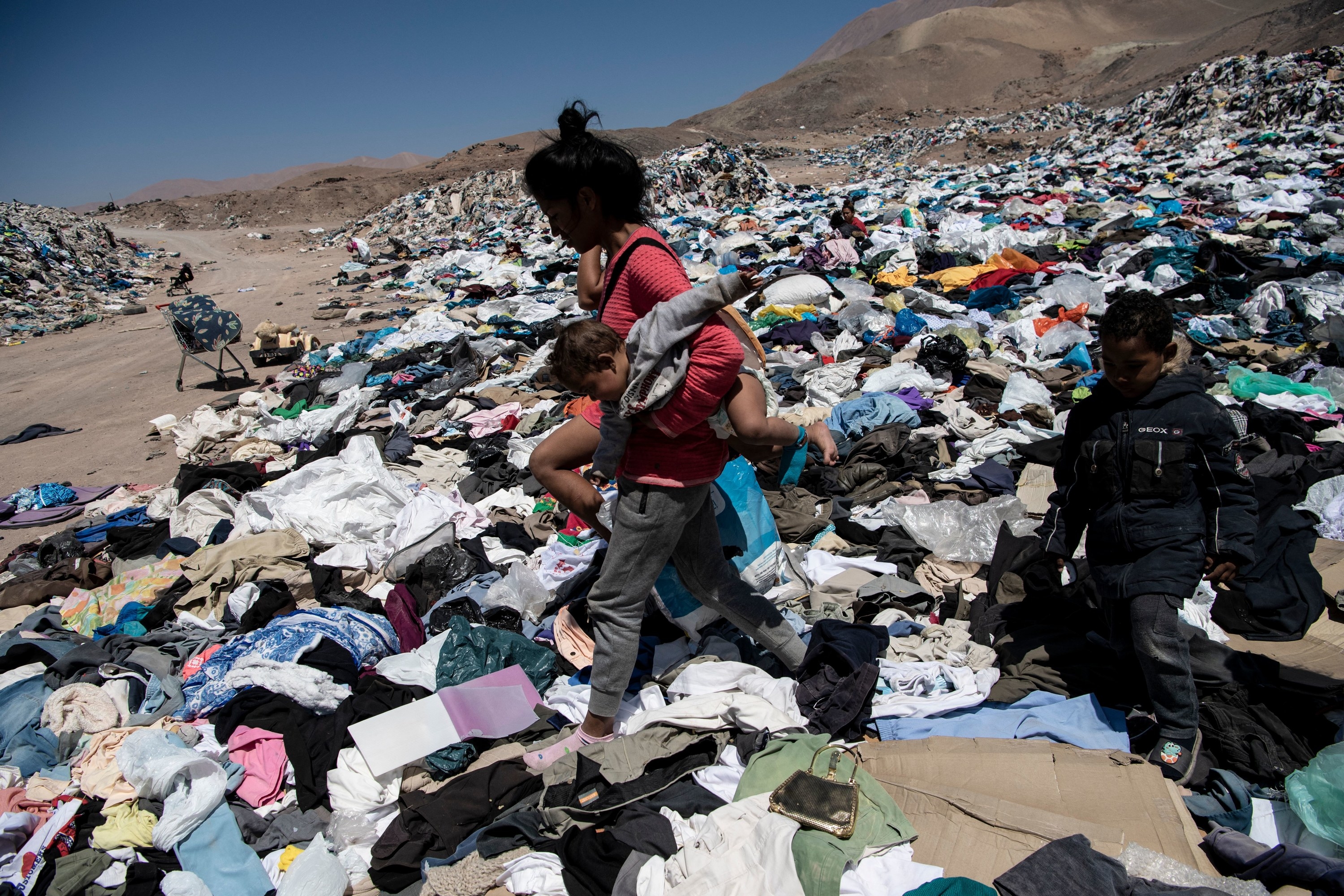 Person carries a child and walks among trash in the desert in South America
