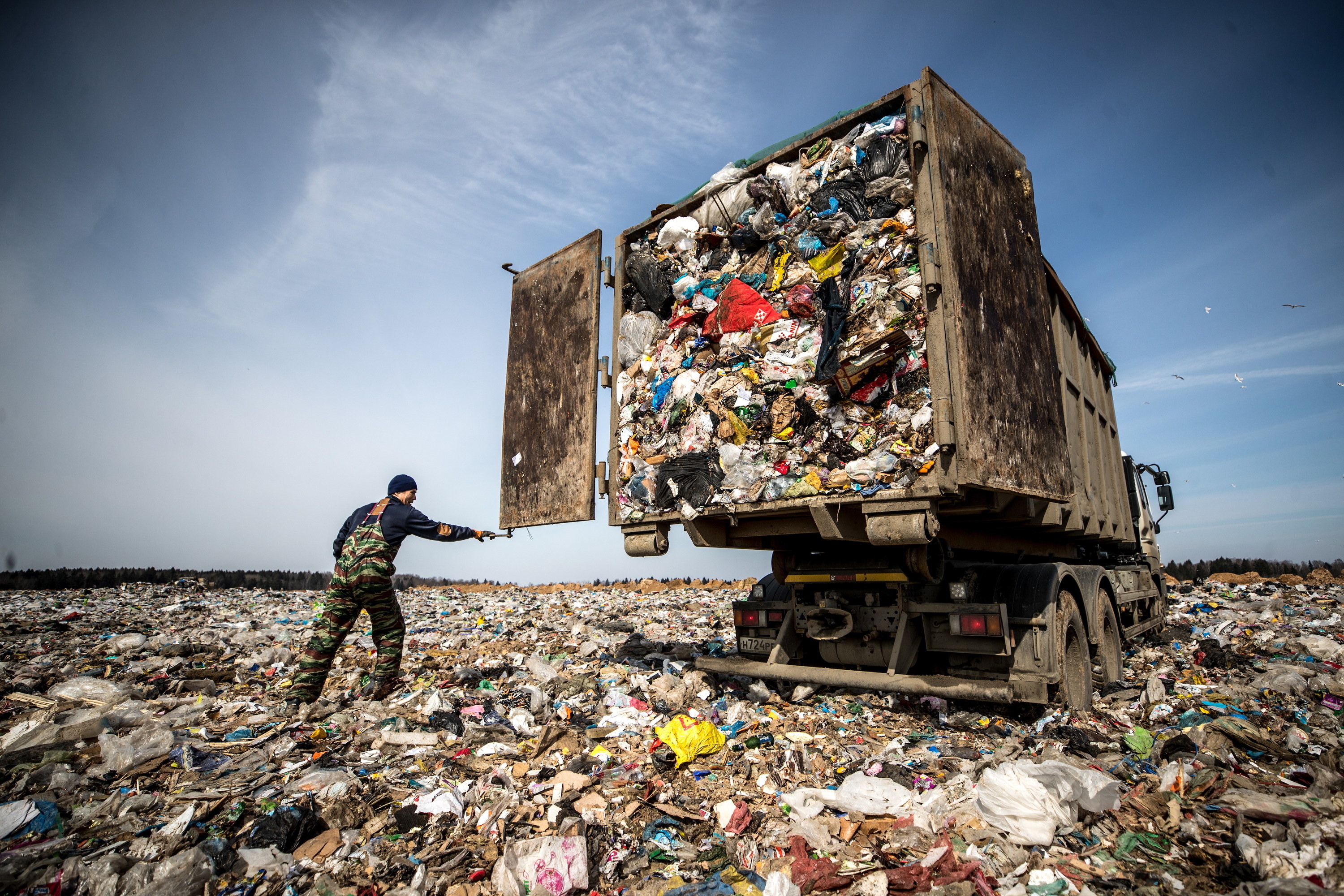 A worker opens the back of a truck for trash to empty into a landfill