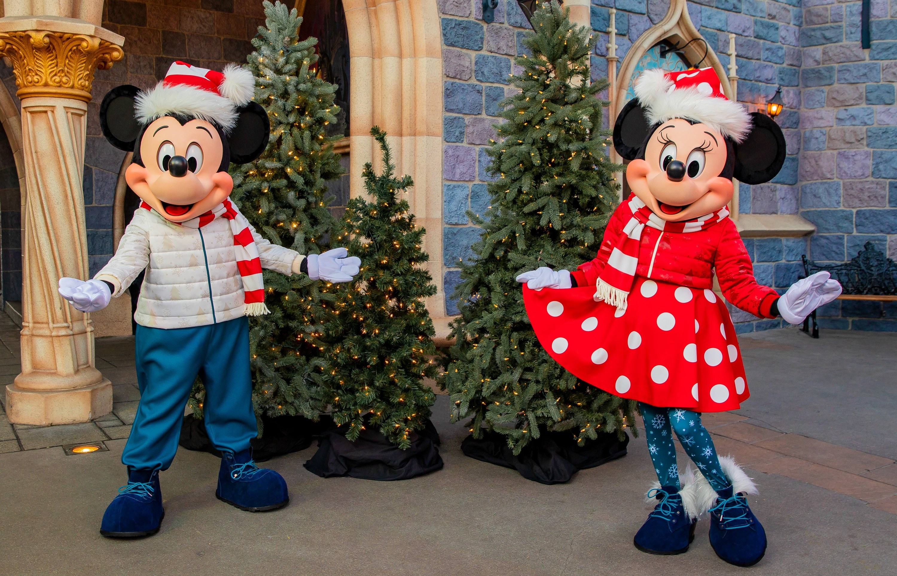 Mickey wearing a white puffy jacket and striped santa hat and Minnie wearing a red puffer jacket and polka dot dress and santa hat