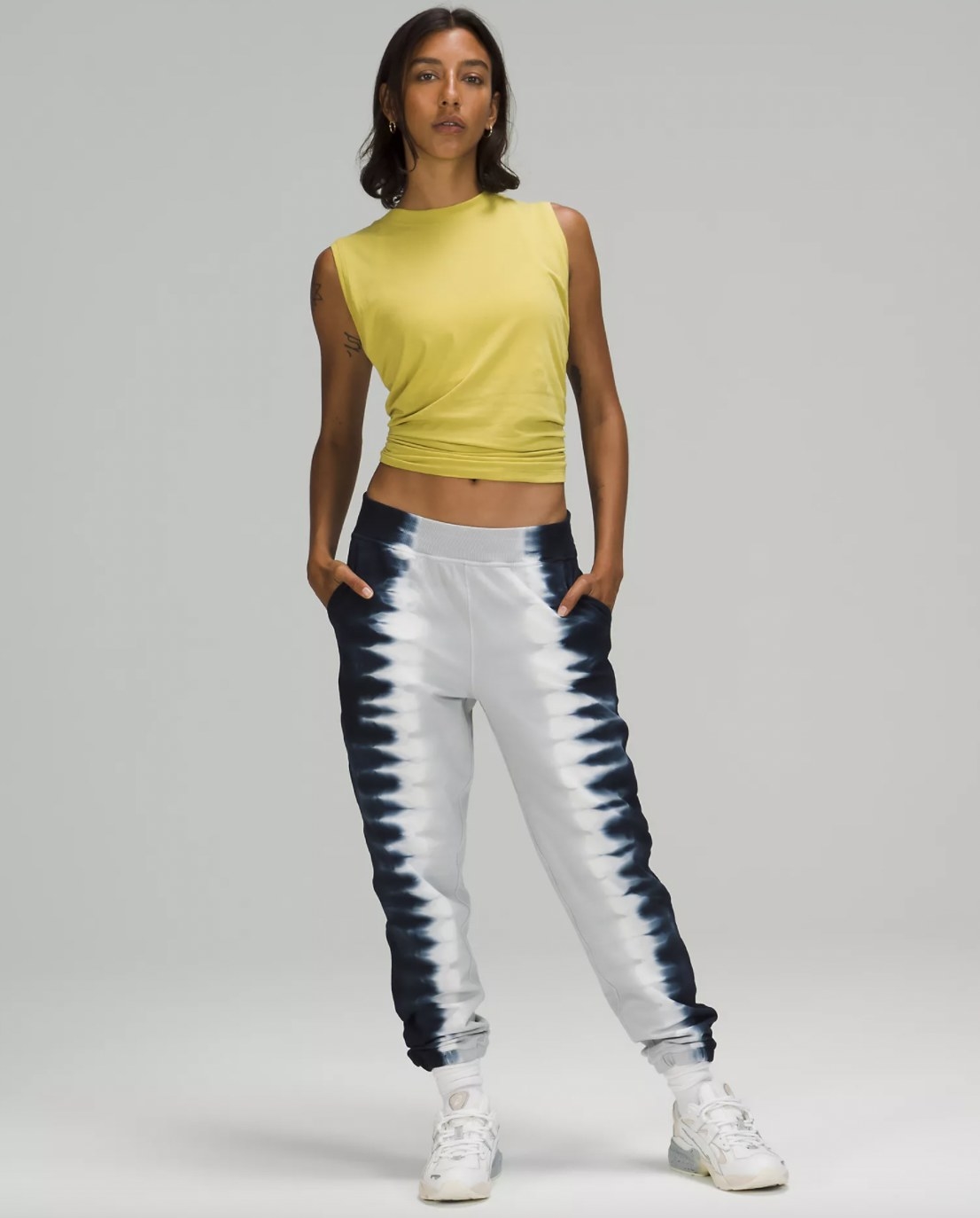 A woman wearing a yellow tank top and white and blue tie-dyed joggers