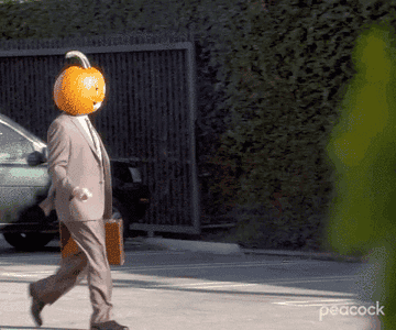 A man with a pumpkin head walks through an office parking lot