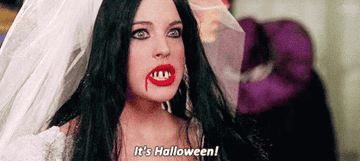 Person with a fake bloody mouth and broken teeth and wearing a bridal veil saying, &quot;It&#x27;s Halloween!&quot;