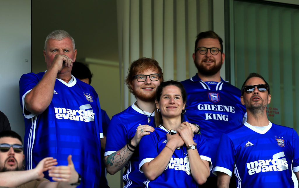 Ed with his arms on his wife Cherry&#x27;s shoulders as they watch a soccer match from the stands