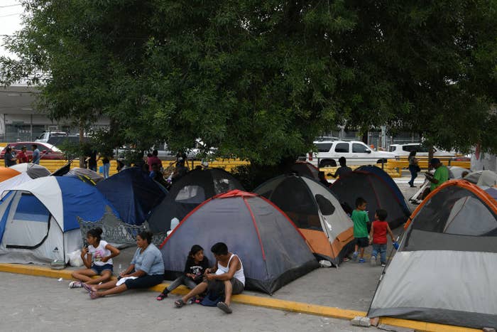 People, including adults and children, sit and stand next to small tents