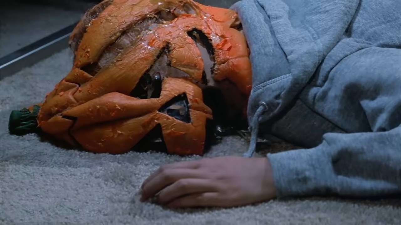A child lies dead wearing a rotting jack-o-lantern mask