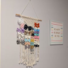 Reviewer's photo of macarame hair accessory holder holding colorful bows and hung on their kids' room wall