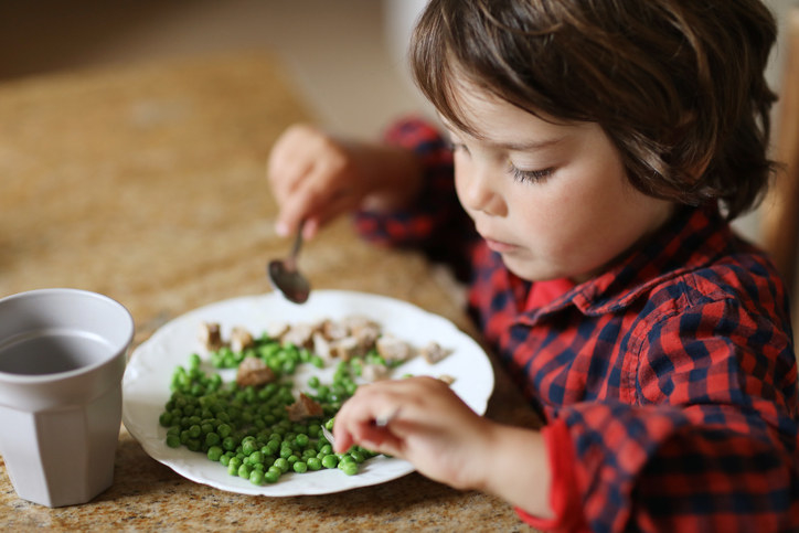 A child with a plate of peas