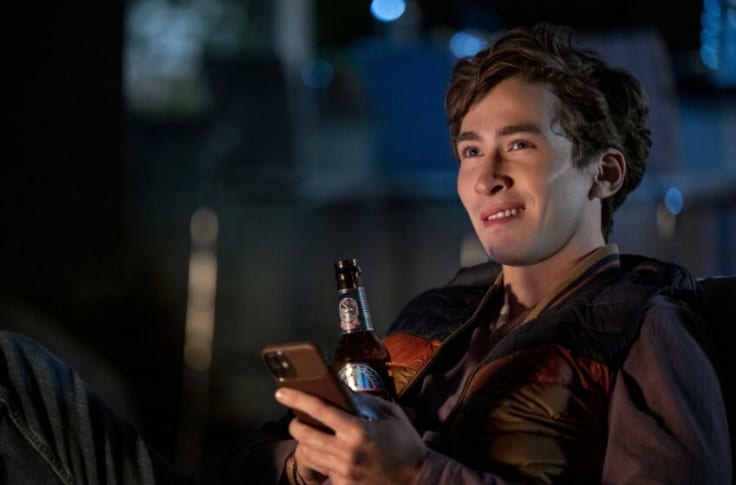 Theo smiling while holding a beer and his phone