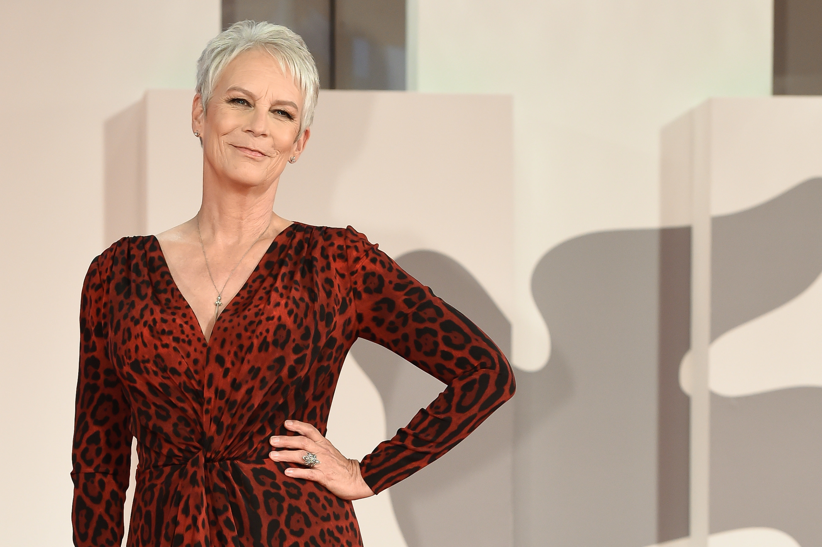 Curtis puts her hand on her hip while wearing a leopard print red dress at a red carpet event