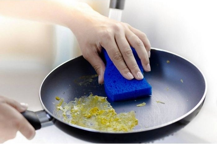Egg being scrubbed out of a nonstick pan using the blue sponge&#x27;s scrubby side