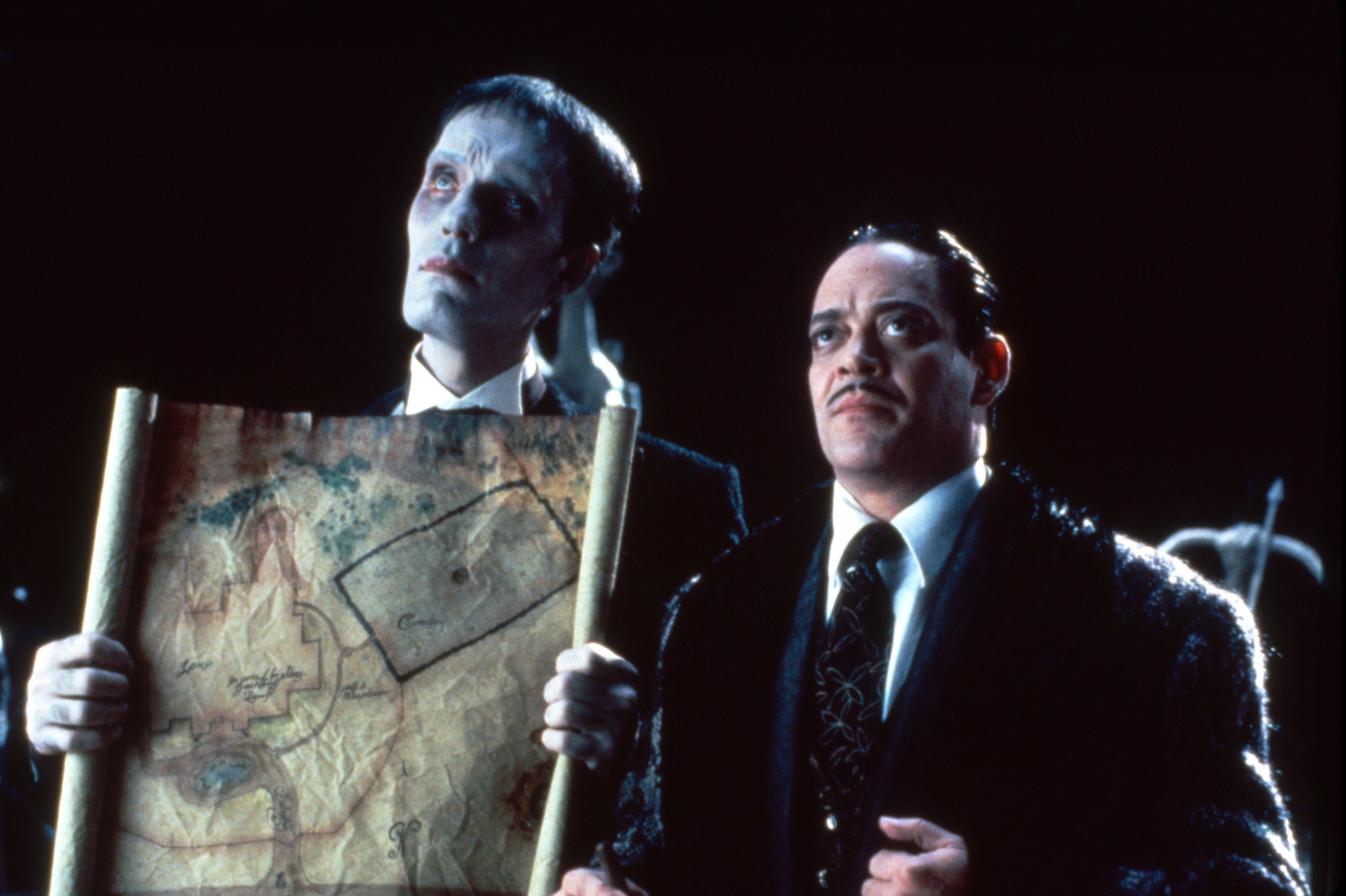 Carel Struycken and Raul Julia hold a map and look up