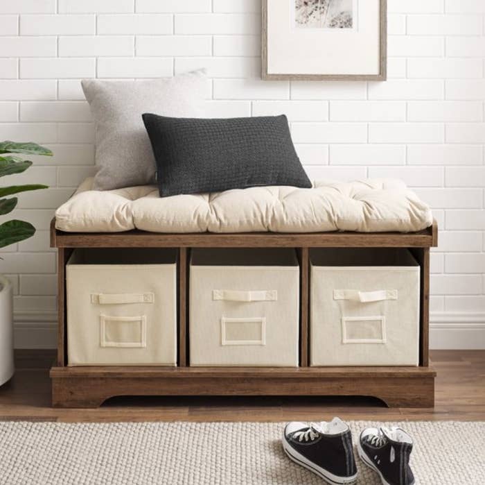 An storage bench with 3 cubbies and a pillow atop in an entryway