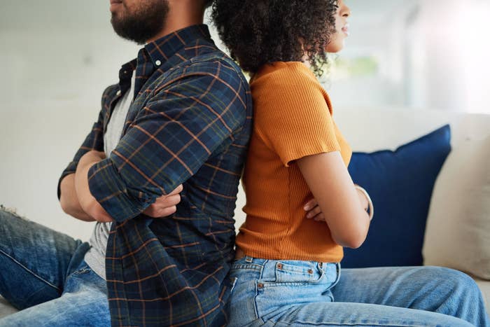 An unhappy couple sit with their arms folded and backs turned away from each other