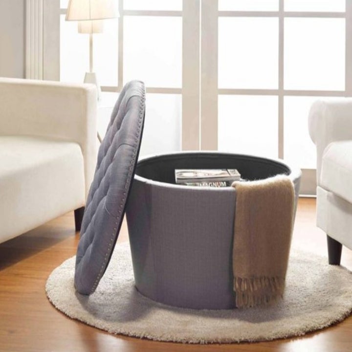 The same ottoman in grey with the lid open displaying the storage inside