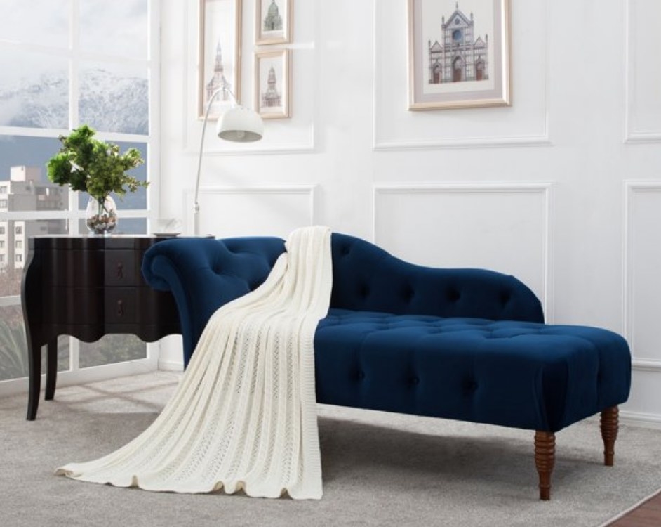 A navy blue tufted, rolled arm chaise lounge with a throw blanket atop
